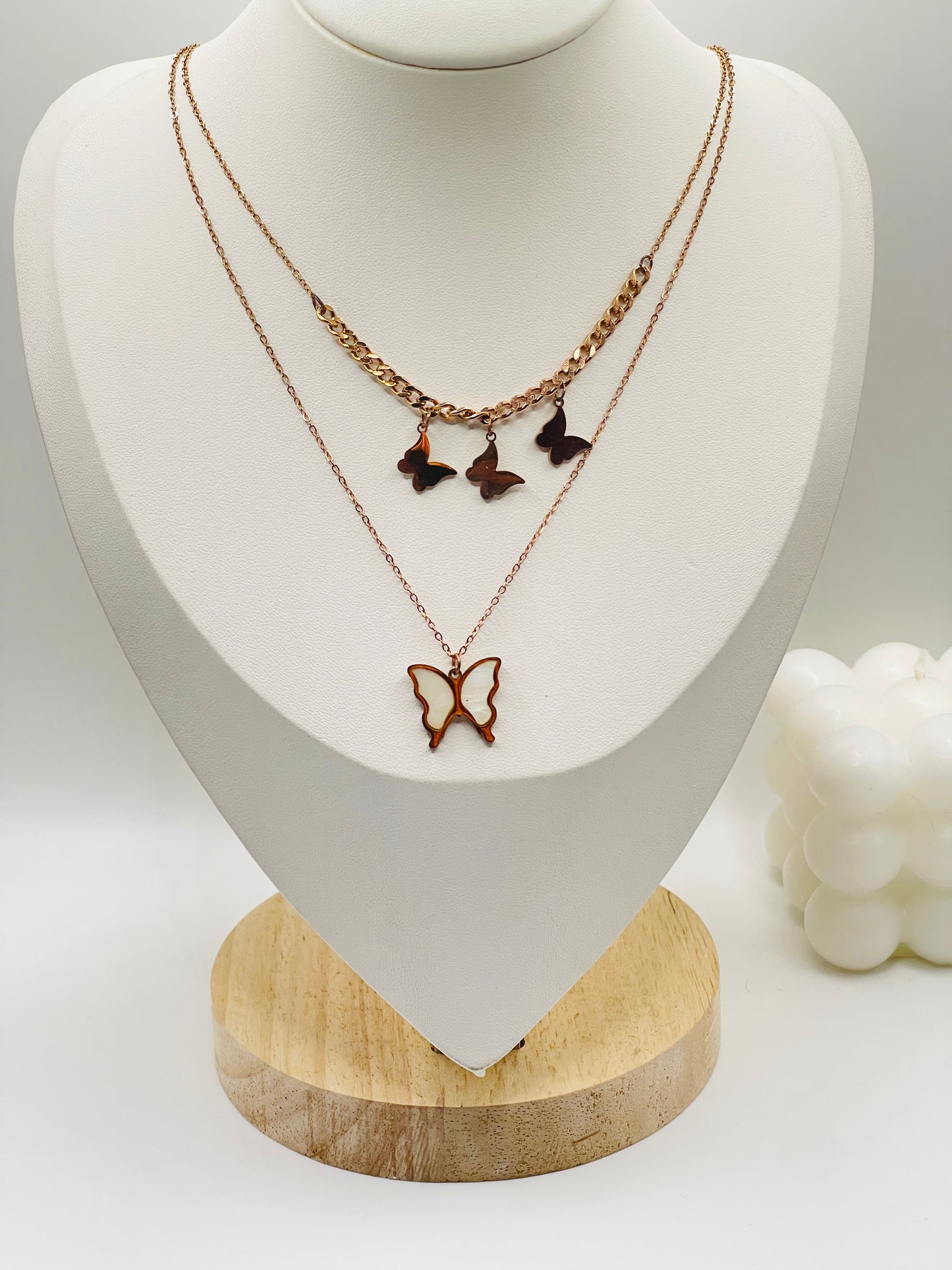 Butterfly-themed necklaces on a white mannequin bust with a wooden base.