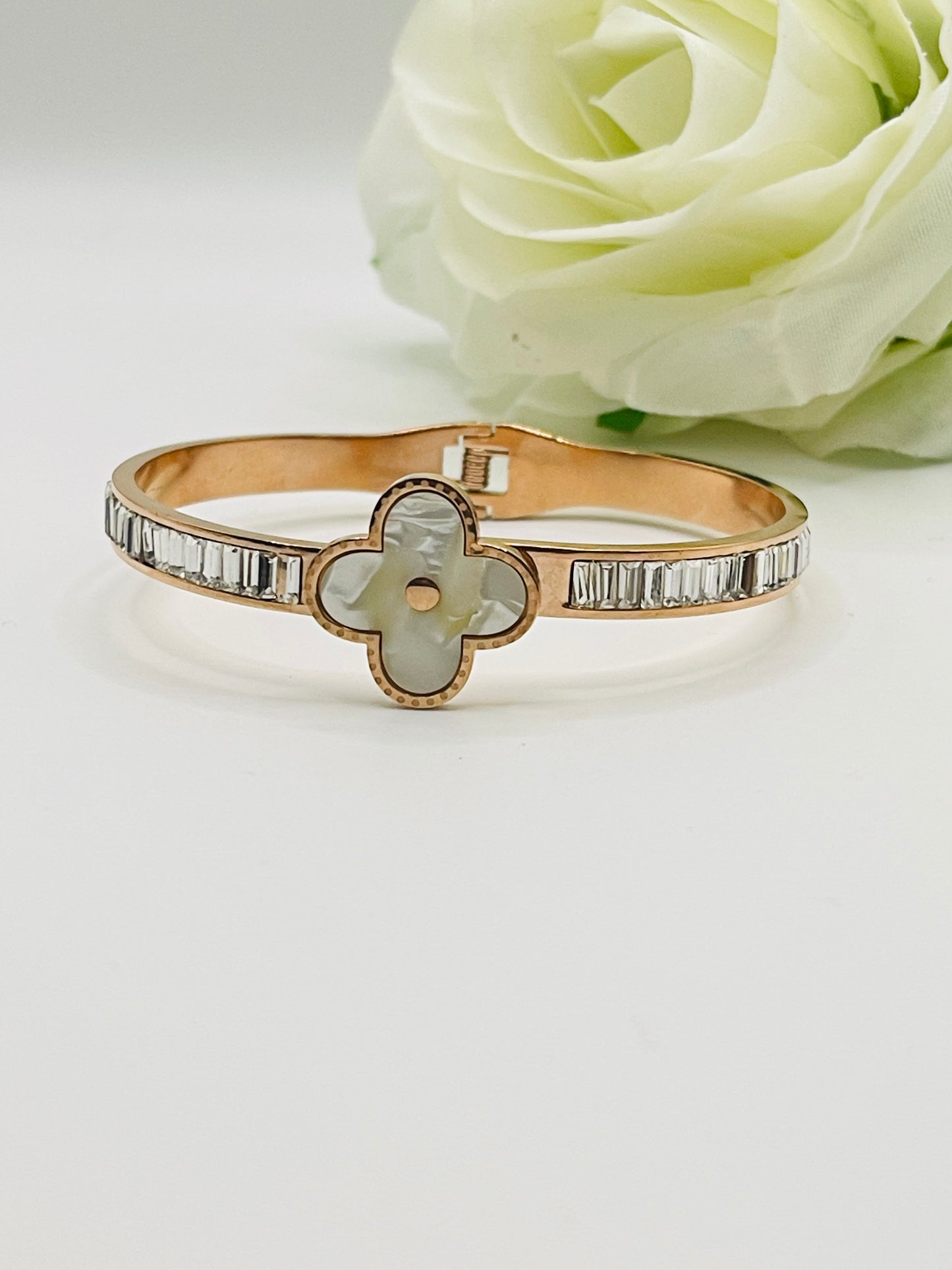 Rose gold bracelet/bangle with a central stone and diamond accents on a white background with a white rose.