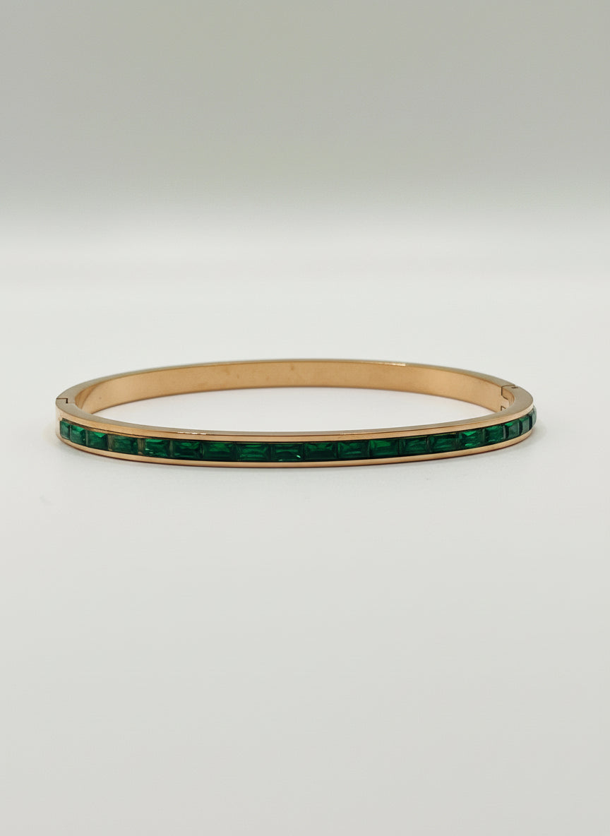 Gold bracelet with green stones on a light gray background with a white rose.