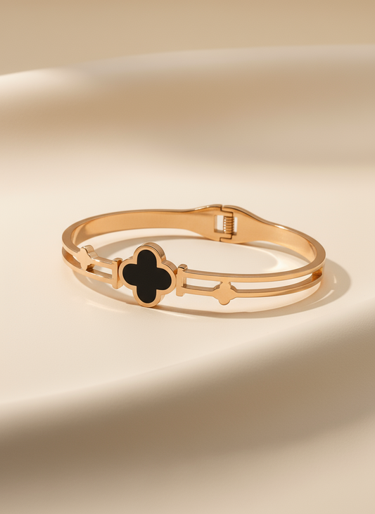 Gold bracelet with a black clover-shaped charm on a beige background