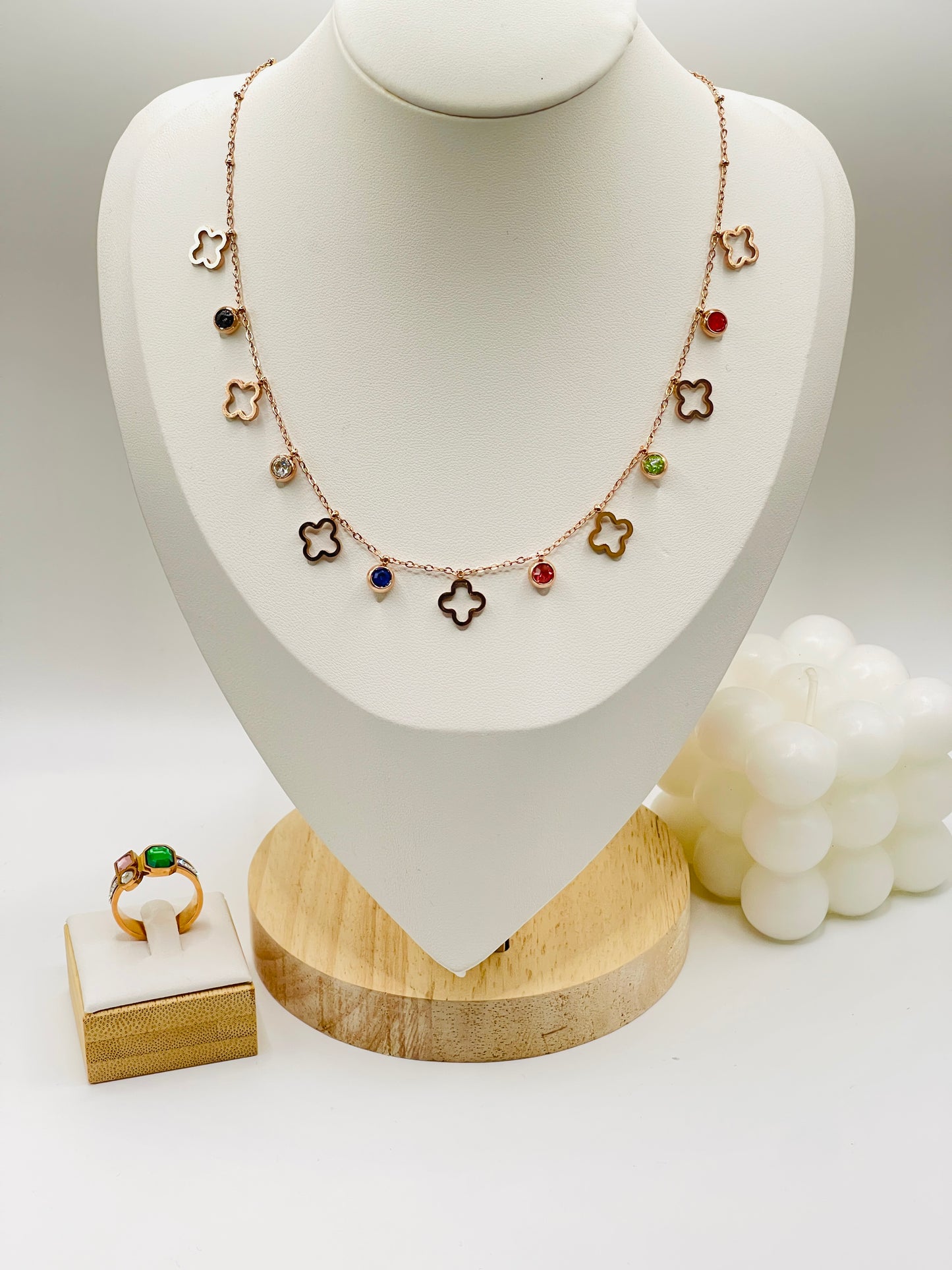 Rose gold Necklace with colorful charms on a white mannequin bust with a ring on a wooden stand.