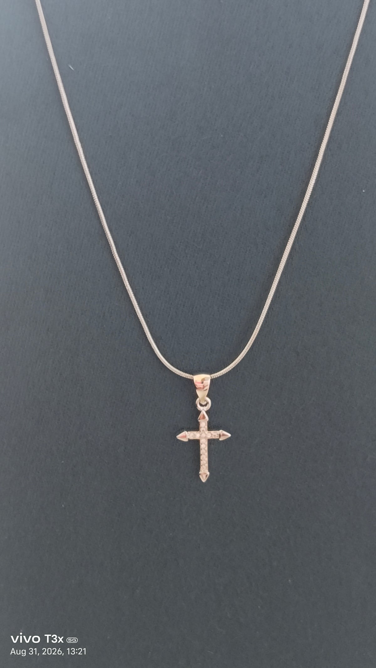 A delicate silver cross pendant necklace on a fine chain, displayed against a dark gray background.