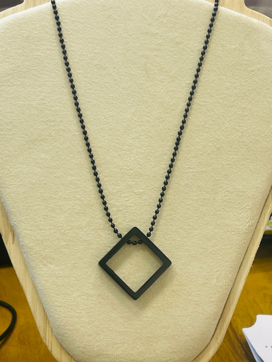A black diamond-shaped pendant necklace with a black beaded chain, displayed on a cream-colored jewelry bust.