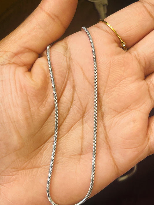 A silver snake chain necklace draped across an open hand, with a gold ring on the index finger.