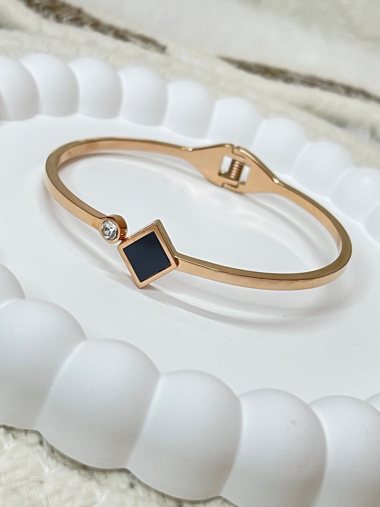 Rose Gold bracelet with a black square stone on a textured white background