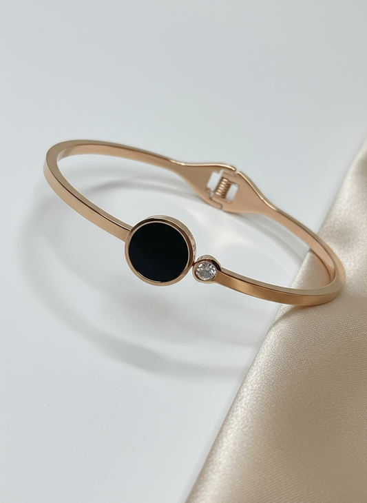 Rose gold bracelet with a black gemstone and clear stone on a light gray background