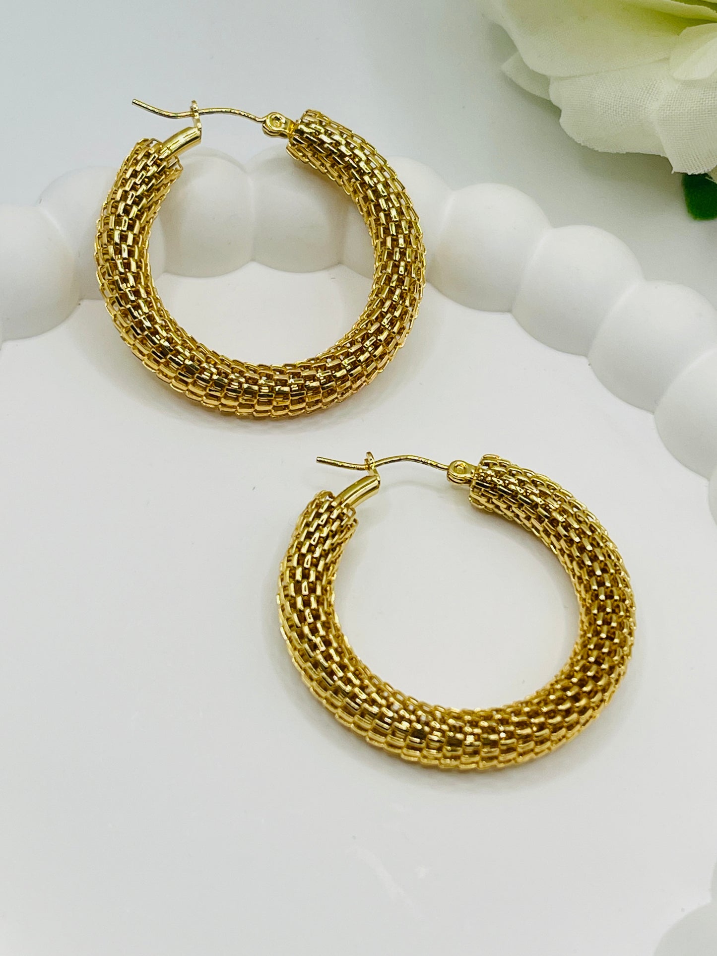 Gold hoop earrings on a white surface with a floral background