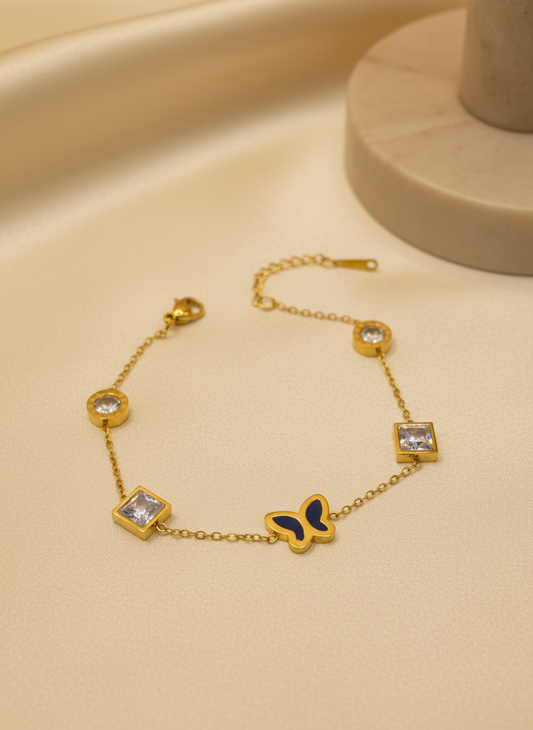 Gold bracelet with butterfly and gemstone details on a beige surface