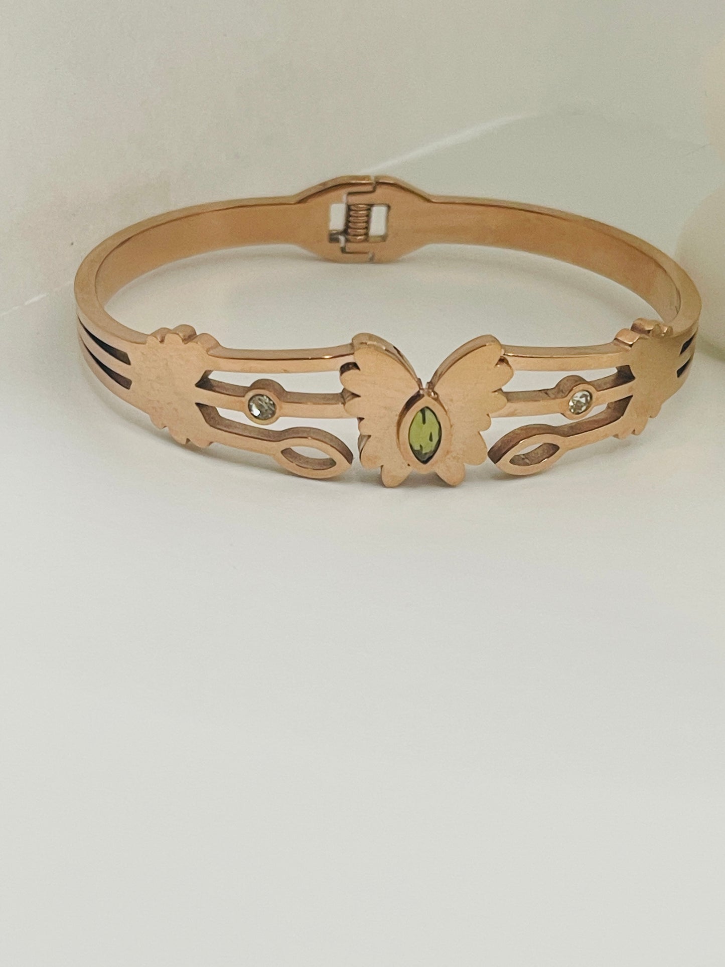 Rose gold bracelet with butterfly design and green gemstone on a white background