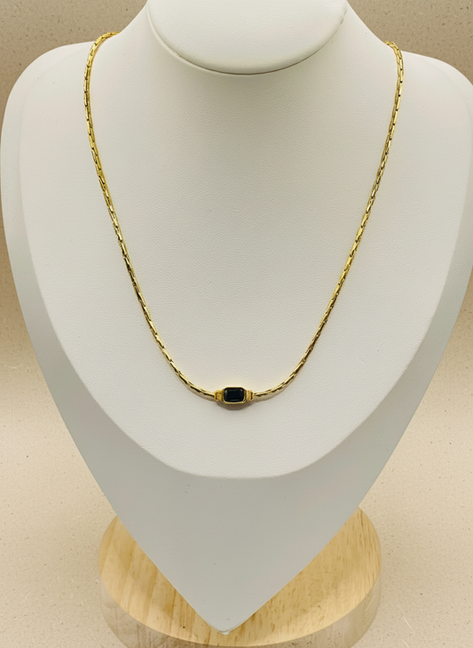 Gold necklace with a black pendant on a mannequin bust.