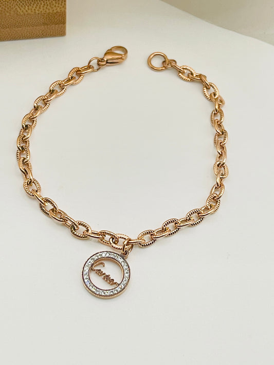 Rose gold bracelet with a circular charm on a white background