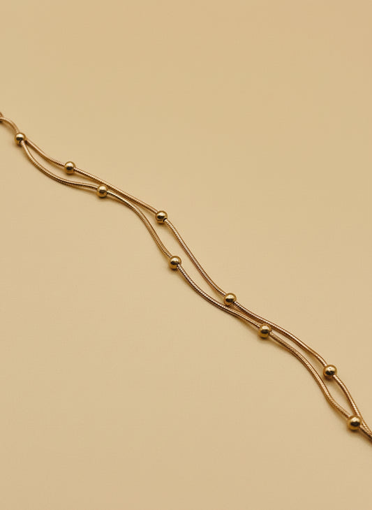 Rose gold chain bracelet on a white surface with a wooden block in the background