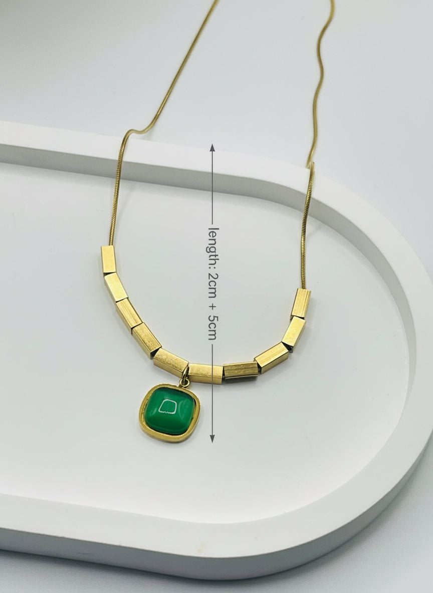 Gold necklace with a green pendant on a white surface