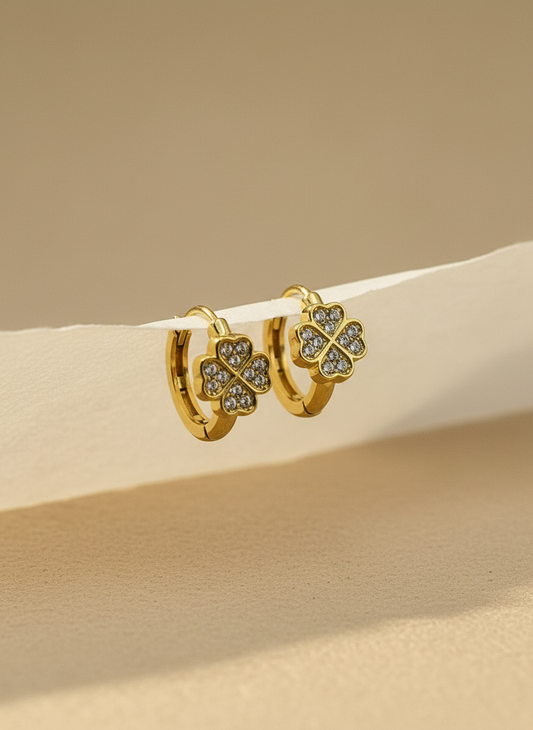 Gold earrings with clover design on a beige surface