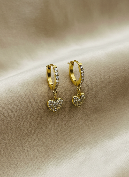 Gold hoop earrings with heart charms on a beige fabric background