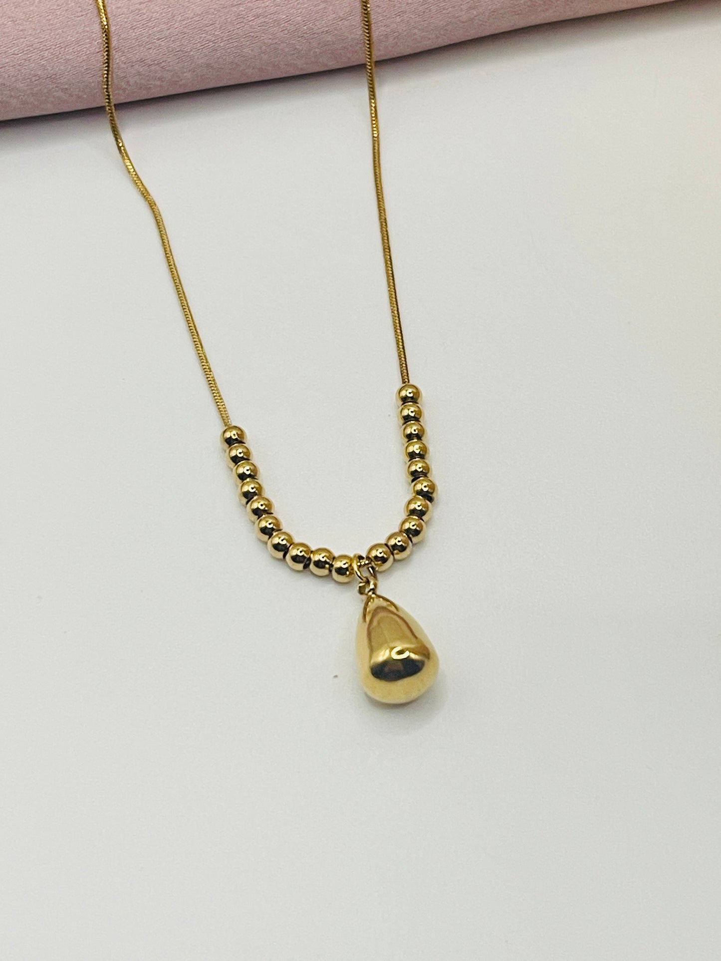 Gold necklace with a heart-shaped pendant on a light pink background