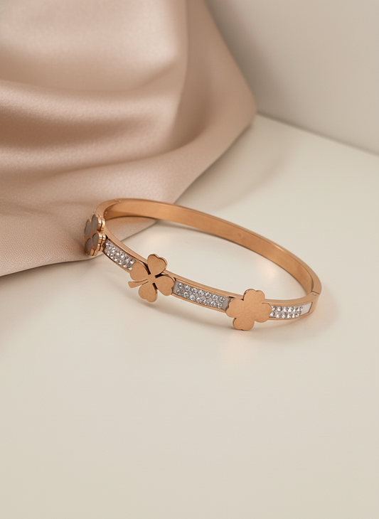 Rose gold bracelet with clover designs on a beige fabric background