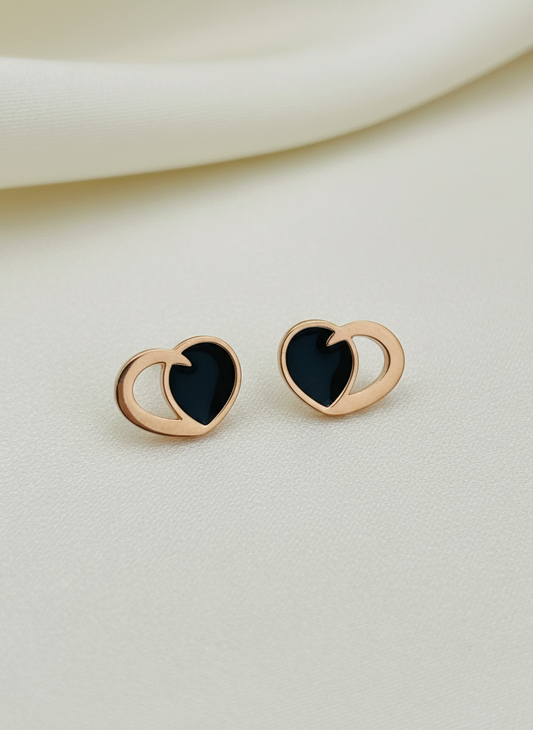 Rose gold heart-shaped earrings with black centers on a beige background