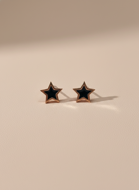 Star-shaped rose gold stud earrings with black centers on a beige background