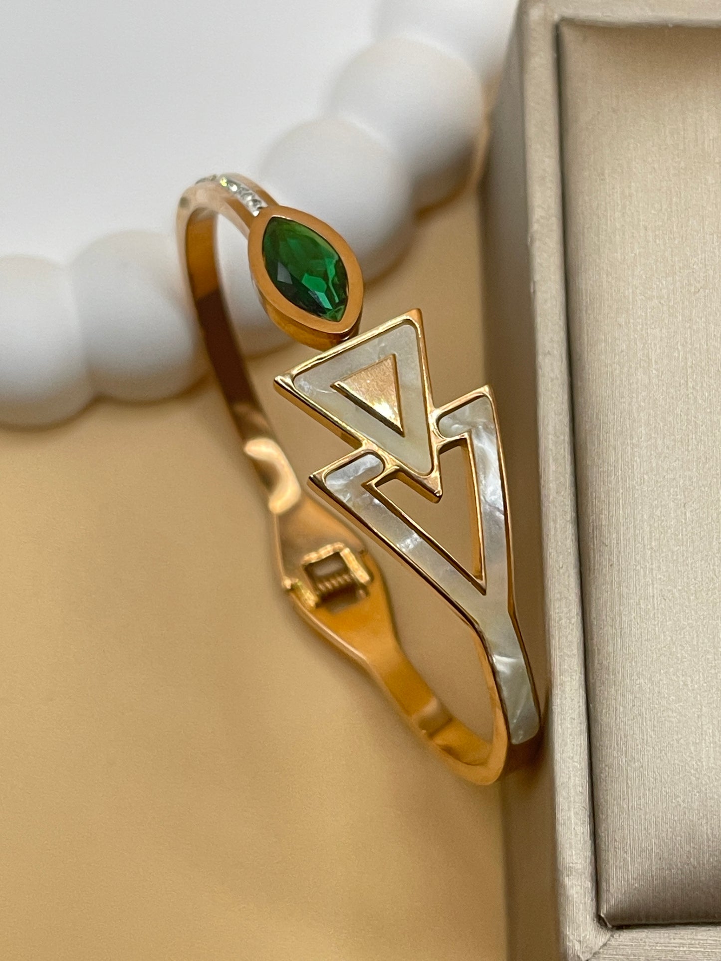 Rose gold bangle with green gemstone and geometric design on a beige background