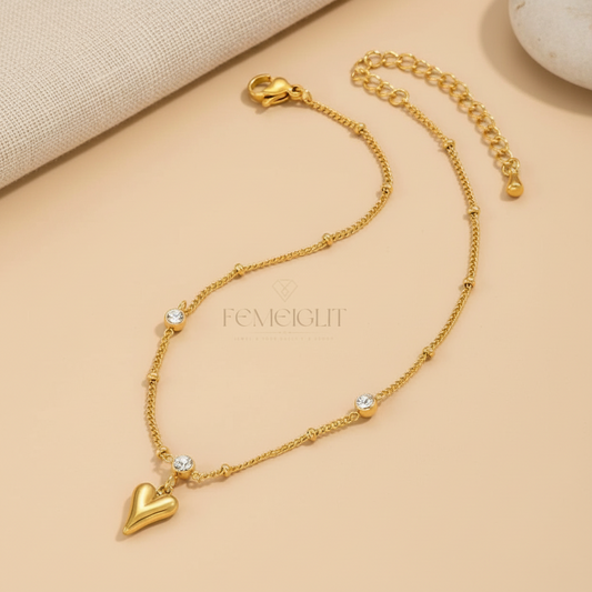 Gold heart-shaped bracelet with small crystals on a beige background