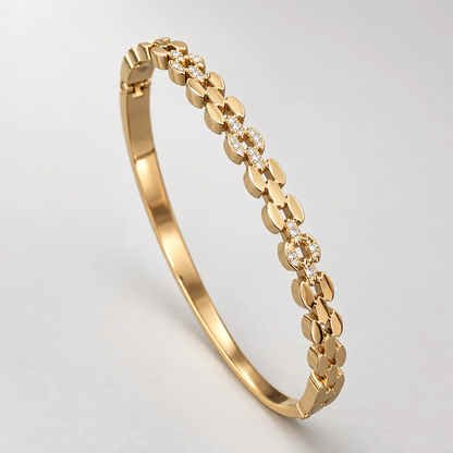 A polished yellow gold hinged bangle bracelet featuring a continuous row of small floral clusters set with clear round-cut gemstones, photographed on a clean light gray background.