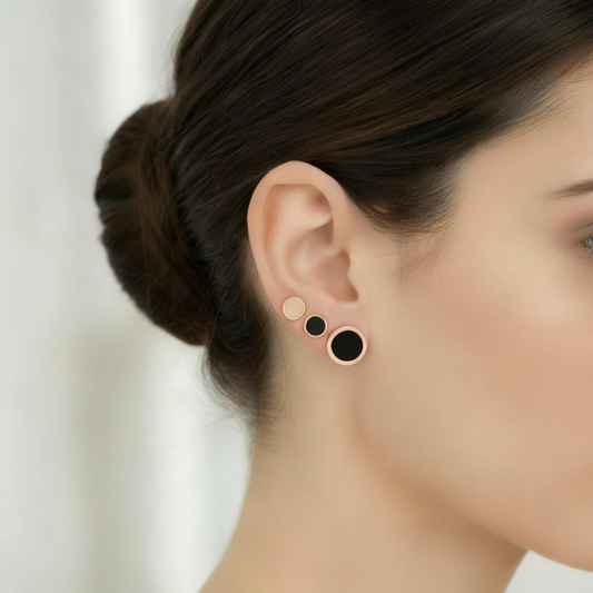 Close-up of a person wearing rose gold earrings with black and pink circular studs on a blurred background