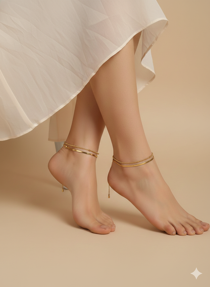 Gold anklets on feet with a white skirt against a beige background