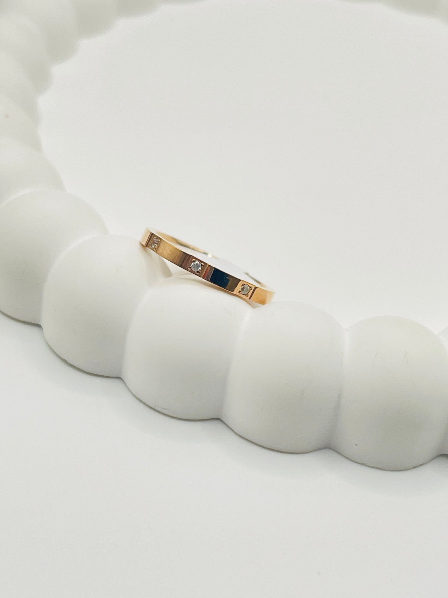 Rose Gold ring with embedded stones on a white ceramic surface