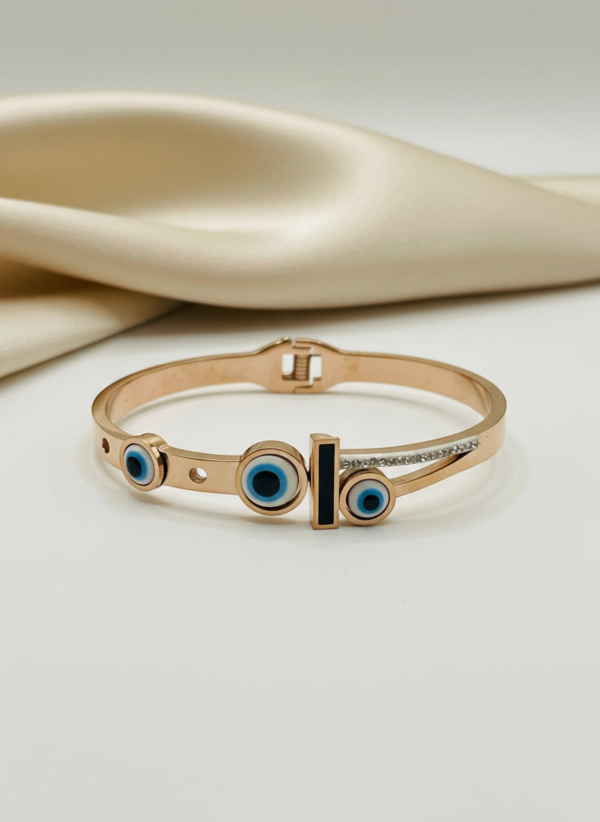 Rose gold bracelet with blue eye design on a white background with a rose.