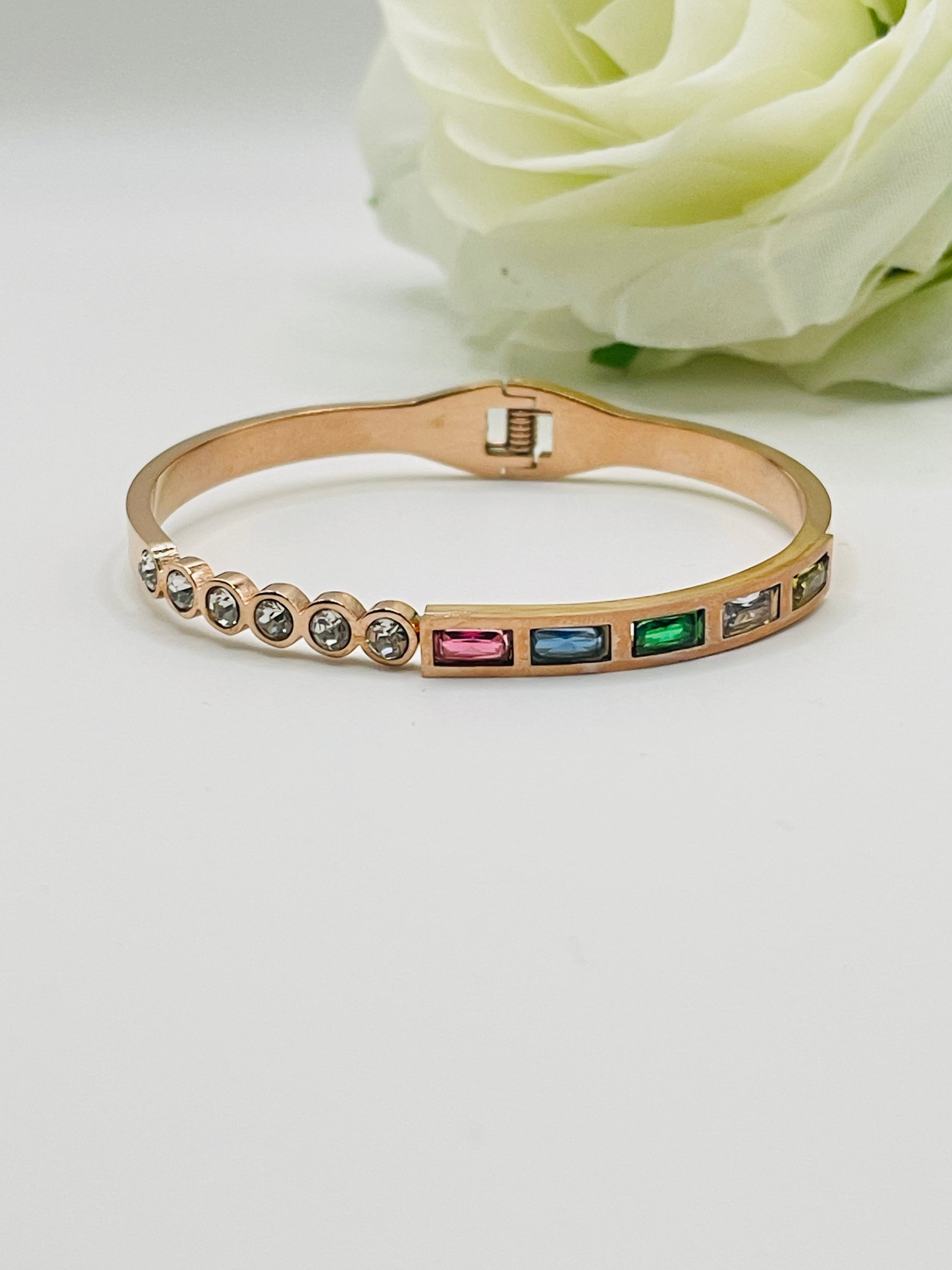 Rose Gold bracelet with colorful stones on a white surface with a white rose in the background