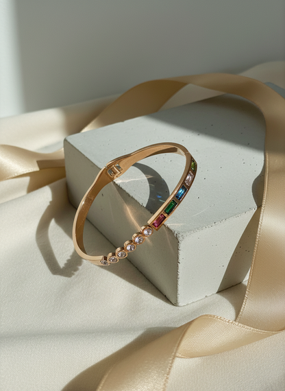 Rose gold bangle with colorful gemstones on a white stand with beige ribbon