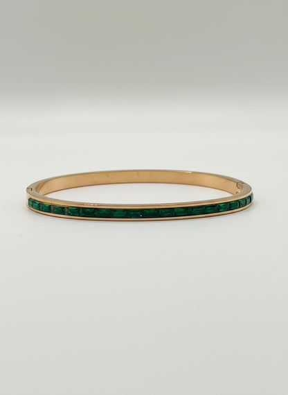 Gold bracelet with green stones on a light gray background with a white rose.