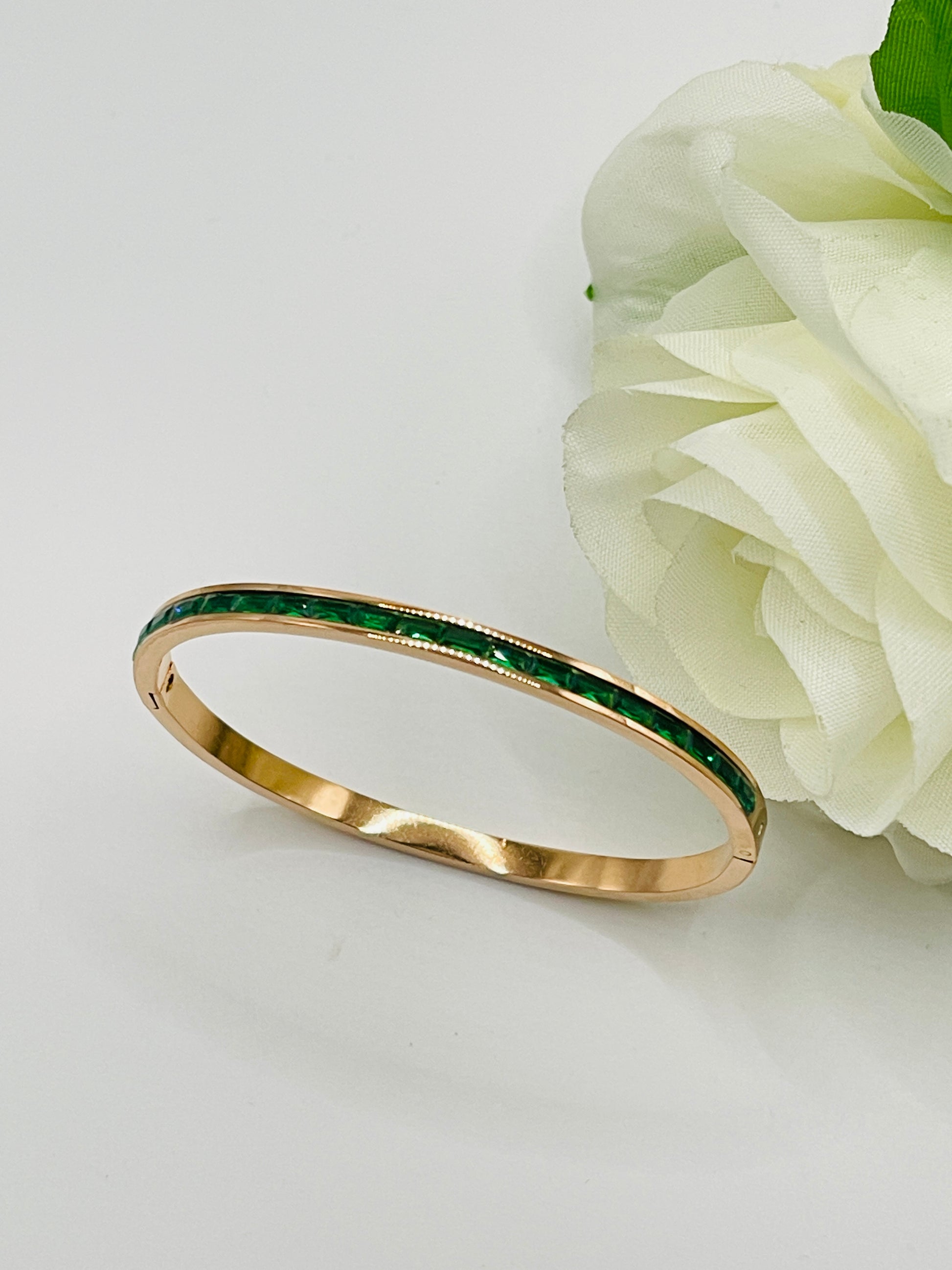 Gold bracelet with green stones next to a white flower on a light gray background