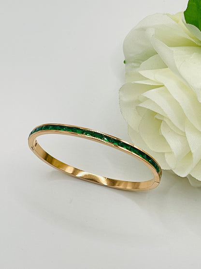 Gold bracelet with green stones next to a white flower on a light gray background