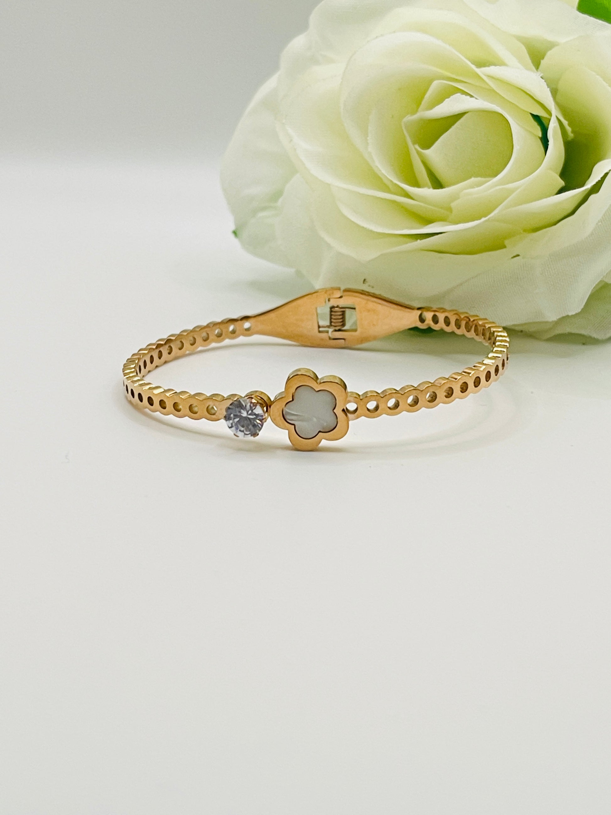 Rose Gold bracelet with a clover design and gemstone on a white surface with a white rose.