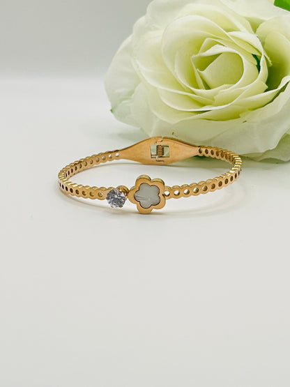 Rose Gold bracelet with a clover design and gemstone on a white surface with a white rose.