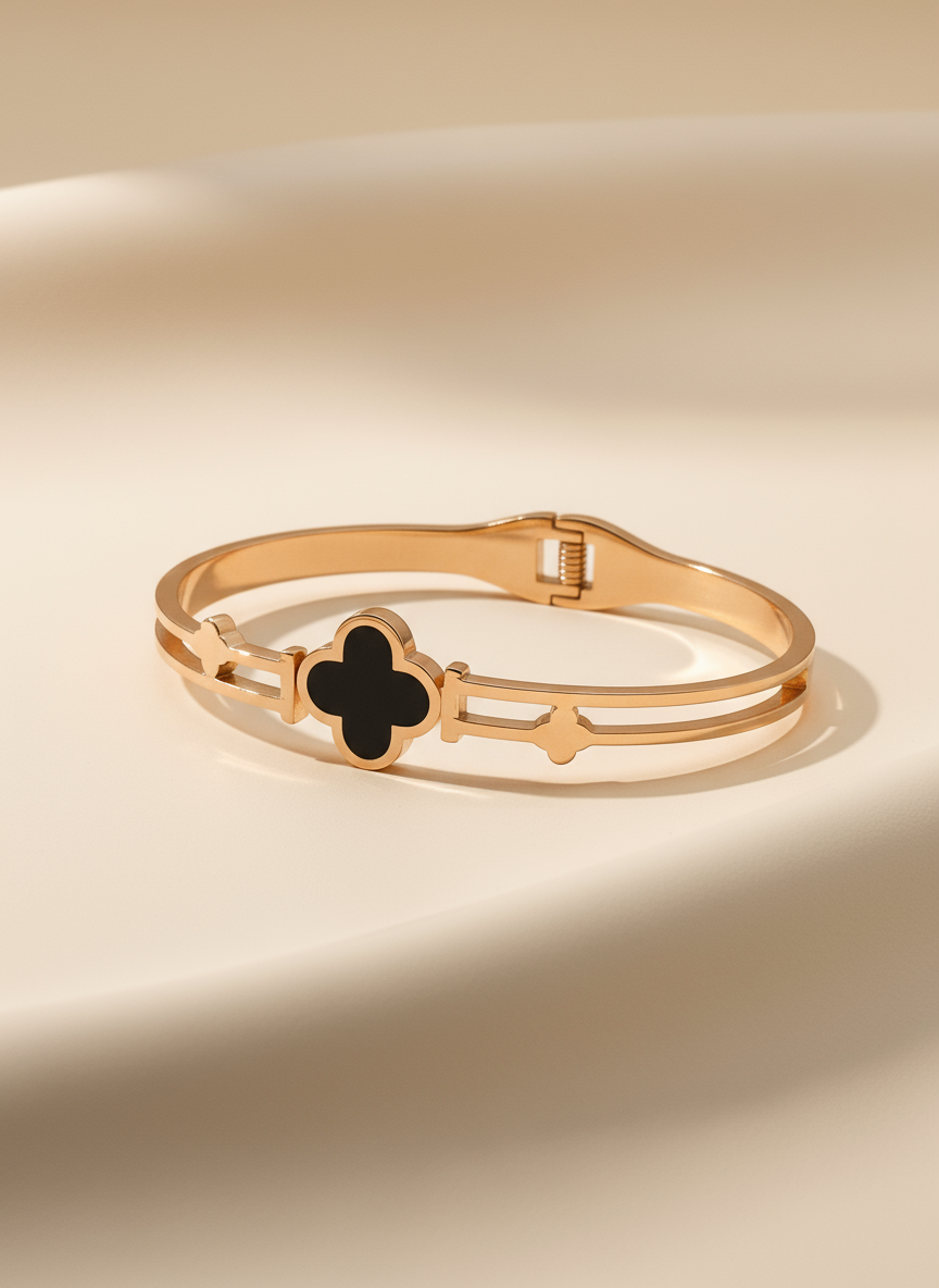 Gold bracelet with a black clover-shaped charm on a beige background