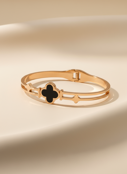 Gold bracelet with a black clover-shaped charm on a beige background