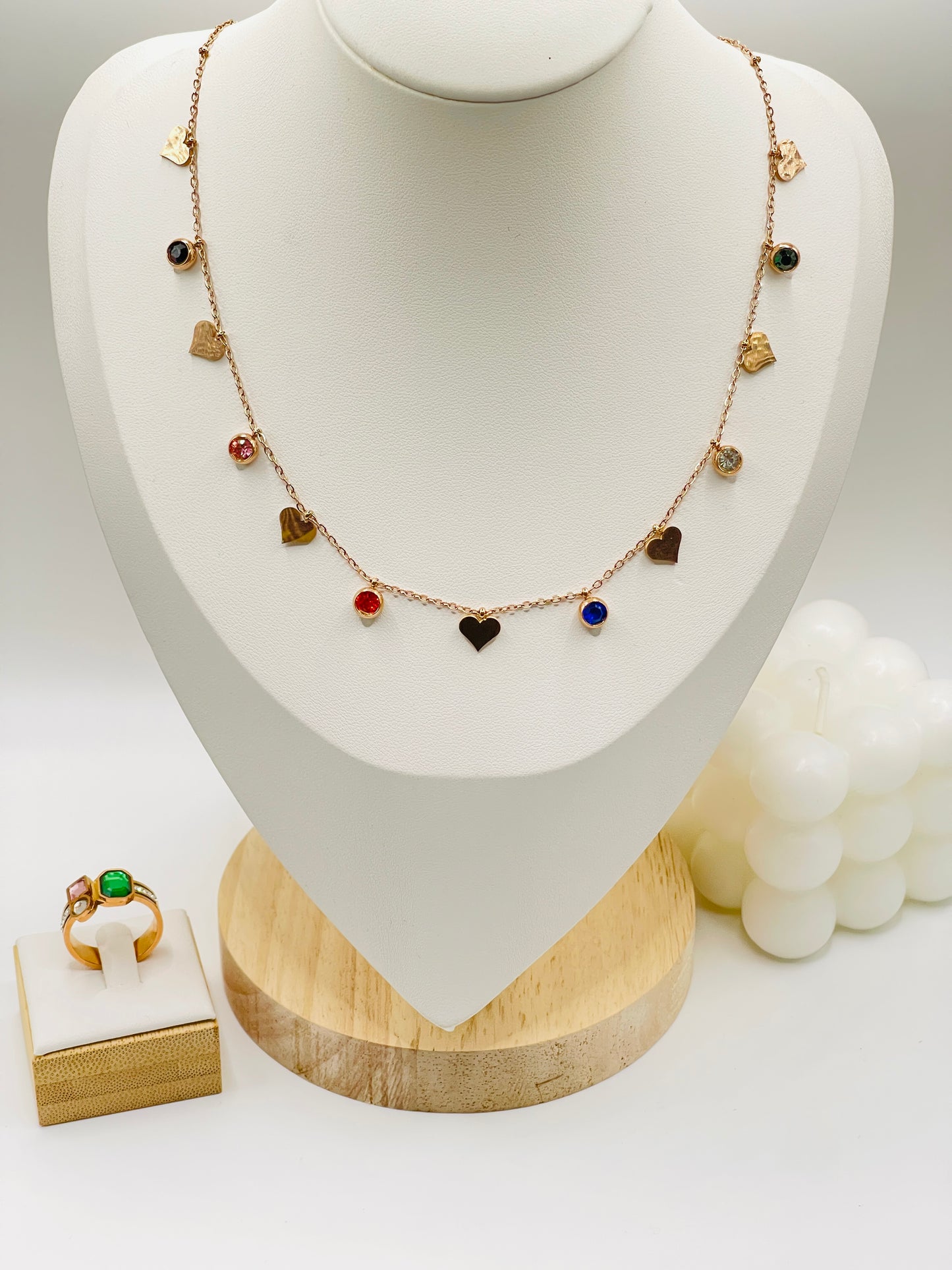 Rose gold Necklace with heart-shaped pendants on a mannequin bust, with a ring on a small stand in the foreground.