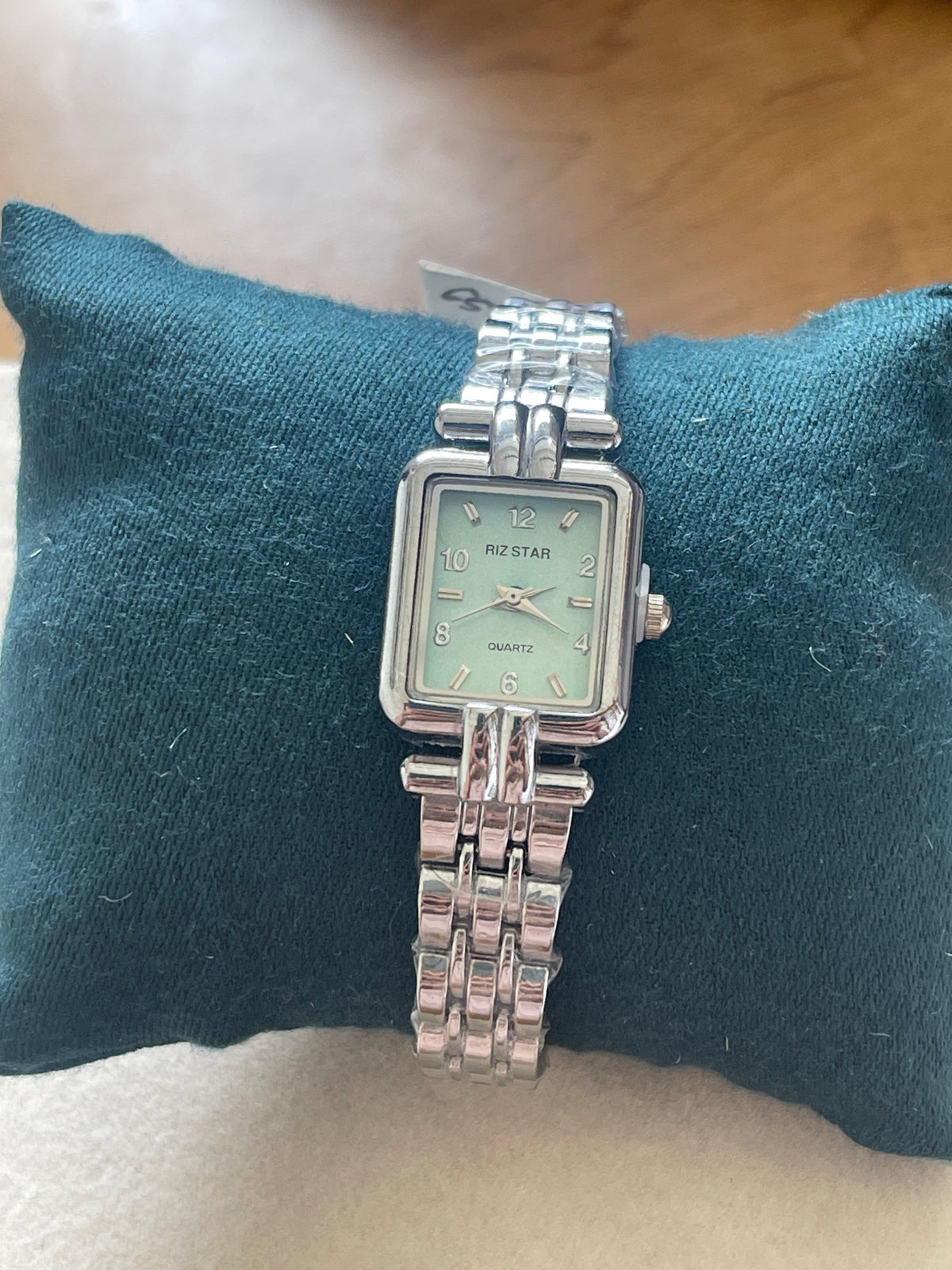 Riz Star square dial mint green quartz watch with silver stainless steel bracelet on teal cushion