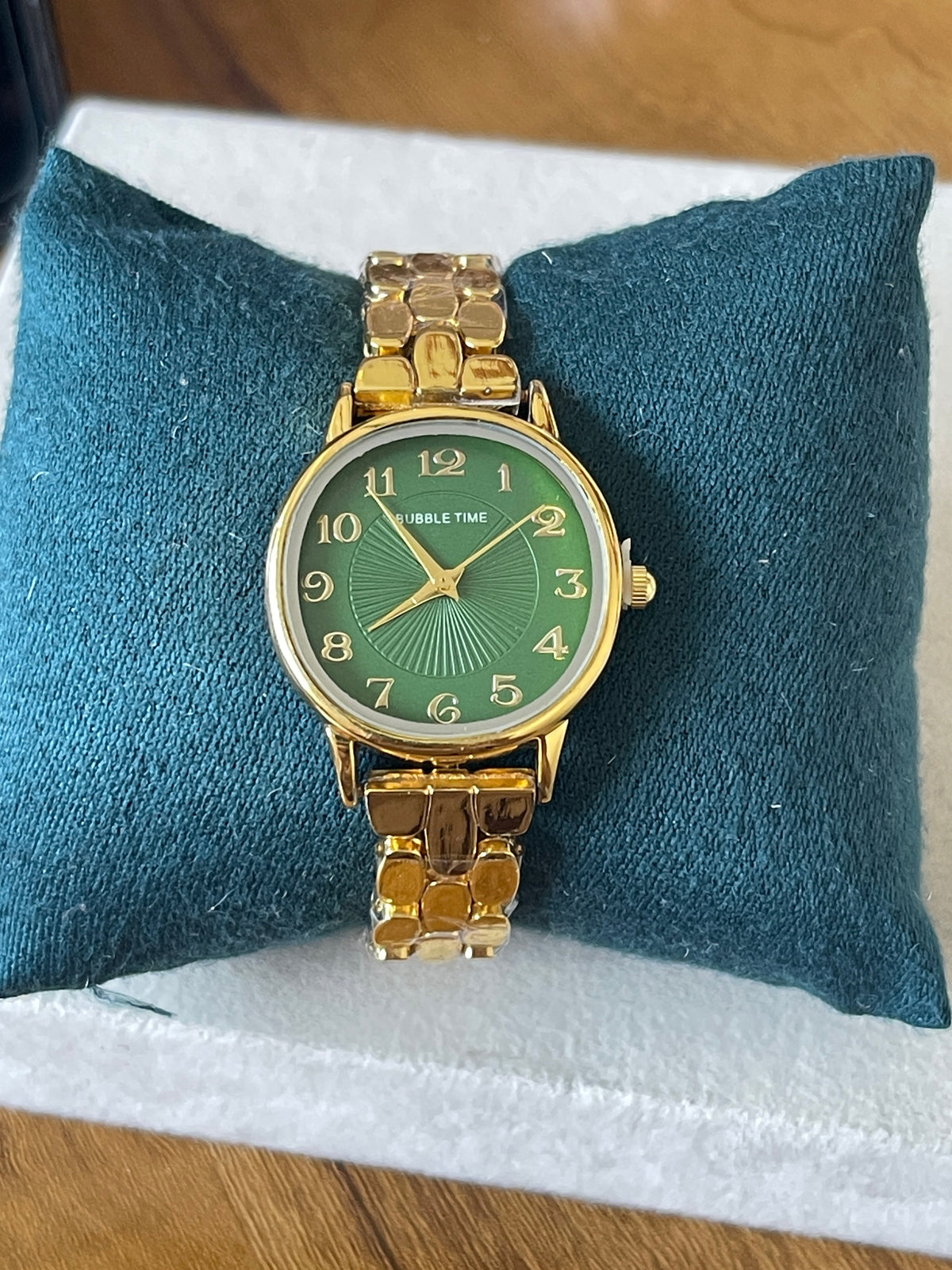 Bubble Time gold bracelet watch with forest green sunburst dial on teal cushion