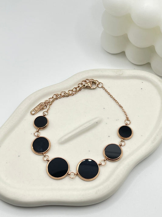 Bracelet with black circular stones and rose gold chain on a white stone surface