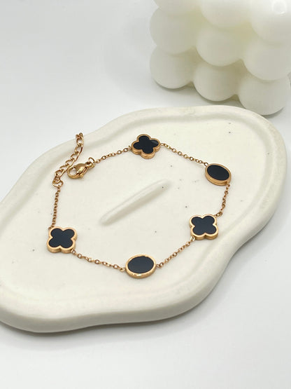 Rose Gold bracelet with black clover-shaped charms on a white stone surface