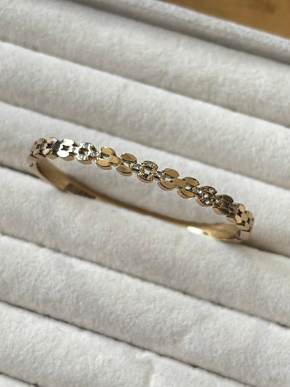 A delicate gold bangle bracelet with a row of small clear stones, displayed on a white textured ring box.