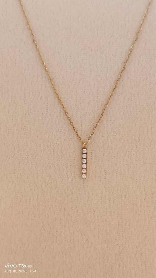 A delicate gold chain necklace with a vertical bar pendant featuring five small clear stones, displayed on a textured beige fabric background.