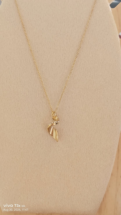 A delicate gold chain necklace with a small leaf-shaped pendant displayed on a beige fabric jewelry bust.
