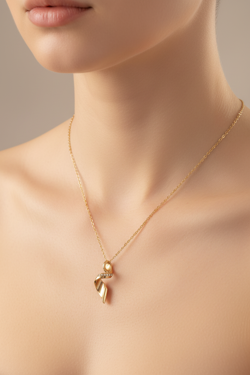 A close-up of a model wearing a delicate gold chain necklace with a small ribbon-shaped pendant and a tiny pearl accent, set against a soft beige background.