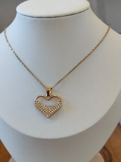 A gold heart pendant necklace with a pavé crystal center, displayed on a white jewelry bust.
