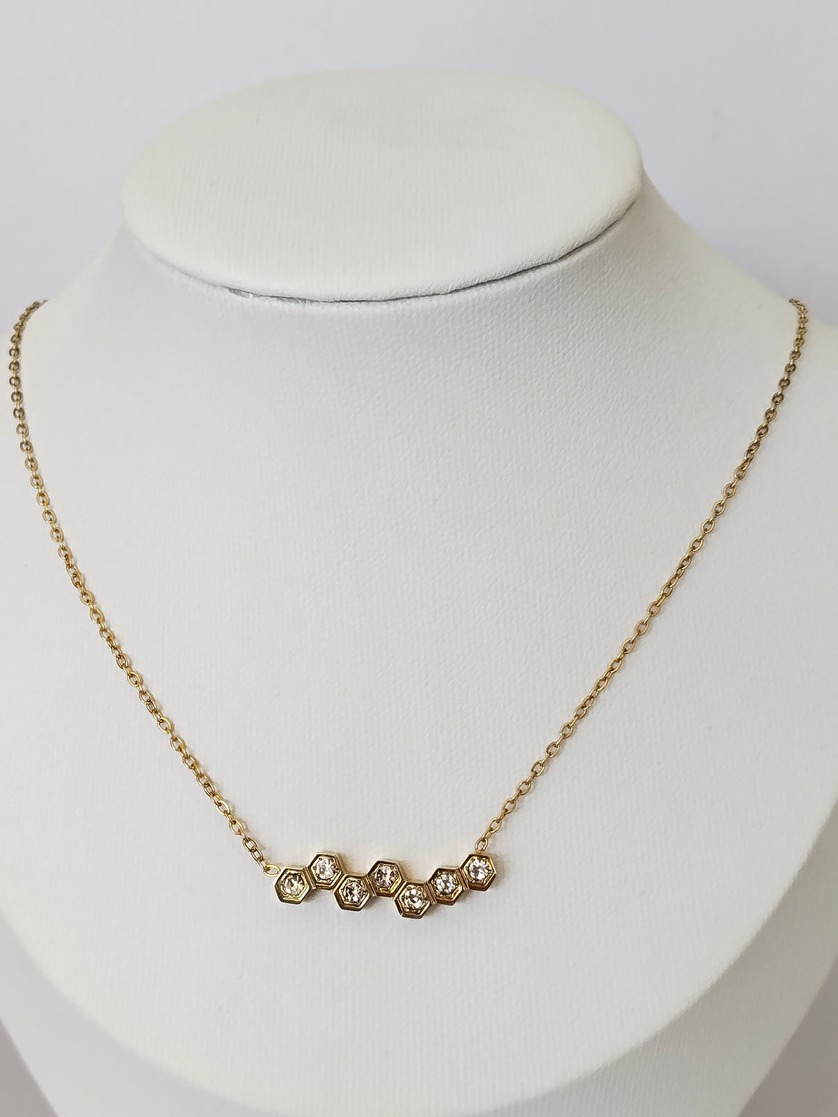 A delicate gold chain necklace with five small, clear, round-cut stones set in a row, displayed on a white jewelry bust.